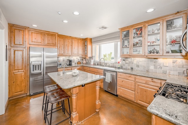 kitchen with sink, a kitchen island, backsplash, appliances with stainless steel finishes, and light stone countertops