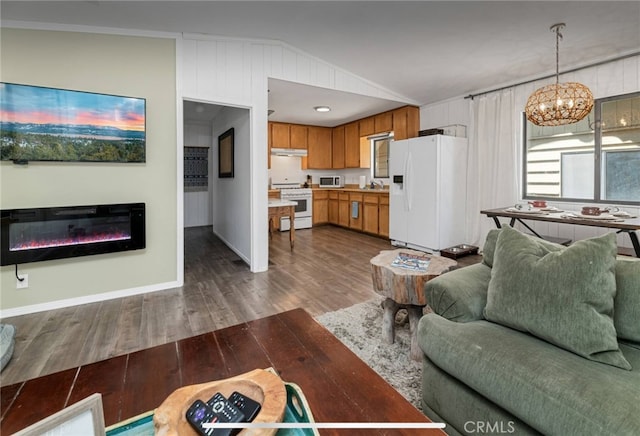 living room featuring dark wood-type flooring, wood walls, lofted ceiling, ornamental molding, and a notable chandelier