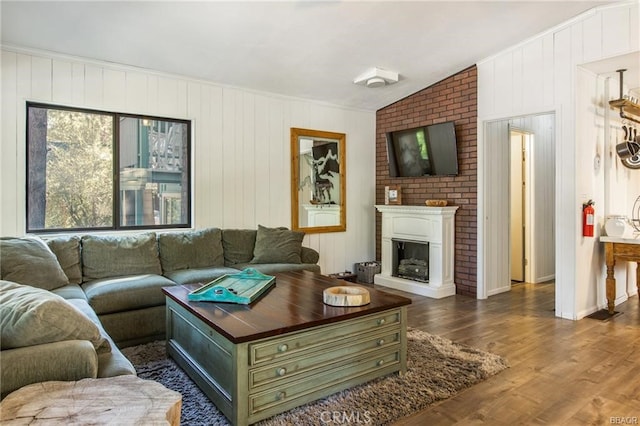 living room featuring vaulted ceiling, a fireplace, dark hardwood / wood-style flooring, crown molding, and wooden walls