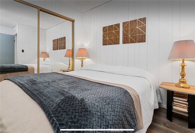 bedroom with wood walls, dark wood-type flooring, and a closet