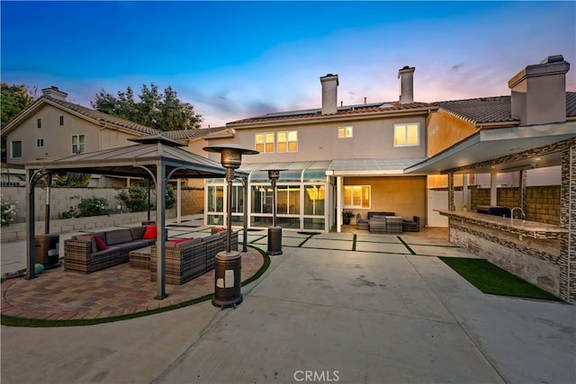 back house at dusk with a gazebo, outdoor lounge area, an outdoor kitchen, and a patio