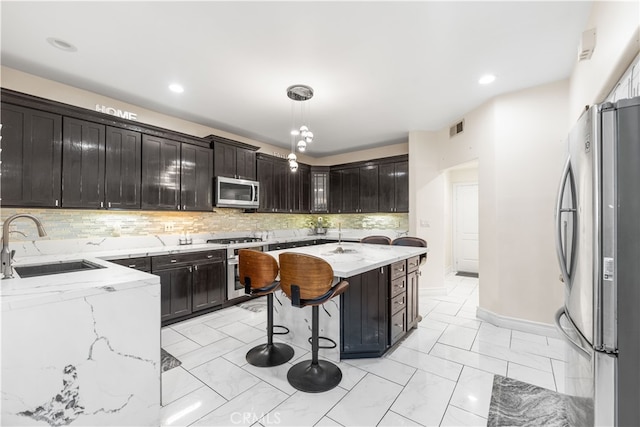 kitchen with decorative light fixtures, sink, stainless steel appliances, light stone countertops, and a center island