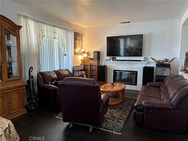 living room with a textured ceiling, a tiled fireplace, and dark hardwood / wood-style floors