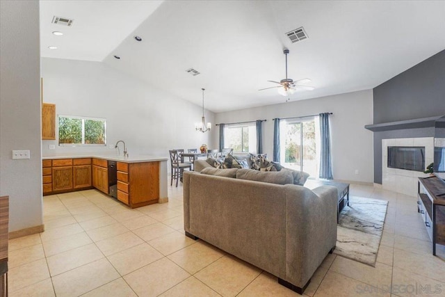 tiled living room featuring ceiling fan with notable chandelier, vaulted ceiling, and a tiled fireplace