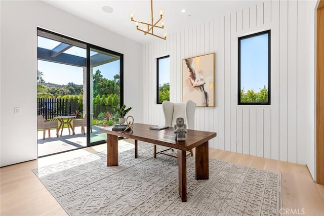 home office with light hardwood / wood-style floors, a wealth of natural light, a notable chandelier, and wood walls