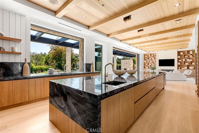 kitchen featuring a large island with sink, light hardwood / wood-style floors, dark stone counters, and sink