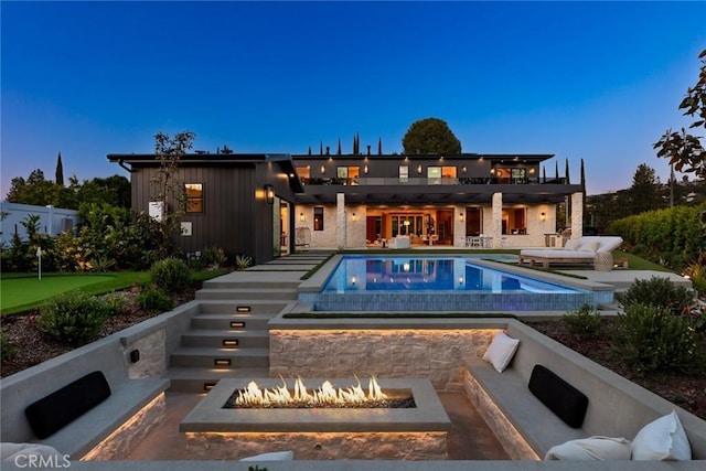 back house at dusk featuring a patio and an outdoor living space with a fire pit