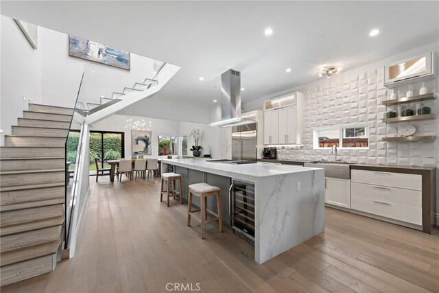 kitchen with island range hood, a kitchen breakfast bar, a large island, sink, and white cabinetry