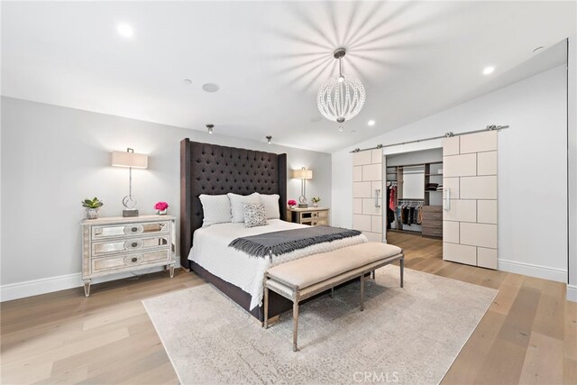 bedroom featuring a spacious closet, lofted ceiling, a barn door, and light wood-type flooring