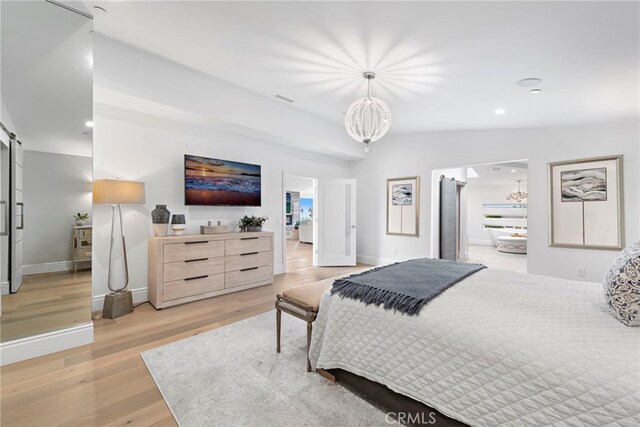 bedroom featuring vaulted ceiling, light hardwood / wood-style flooring, a chandelier, and a barn door