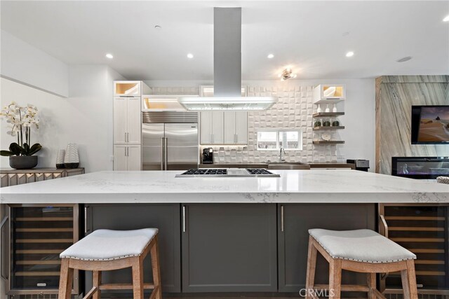 kitchen with beverage cooler, light stone countertops, island range hood, gray cabinets, and stainless steel appliances