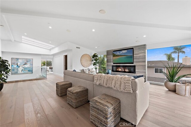 living room featuring lofted ceiling with beams, a large fireplace, and light wood-type flooring