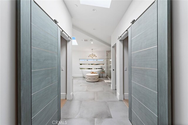 hallway featuring an inviting chandelier, a skylight, and a barn door