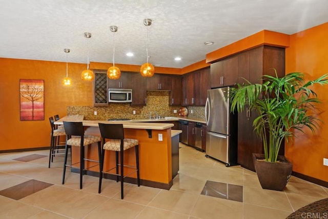 kitchen featuring appliances with stainless steel finishes, backsplash, a breakfast bar area, decorative light fixtures, and dark brown cabinetry