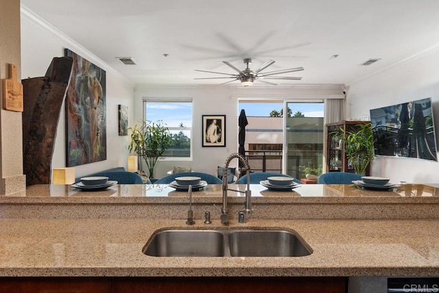 kitchen with ceiling fan, ornamental molding, light stone countertops, and sink