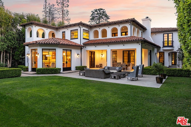 back house at dusk featuring a patio, an outdoor living space, and a lawn