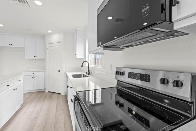 kitchen featuring sink, white cabinetry, stainless steel electric range oven, and light hardwood / wood-style flooring