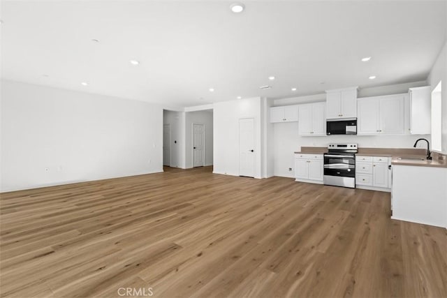 kitchen with sink, white cabinets, light hardwood / wood-style flooring, and stainless steel range with electric stovetop