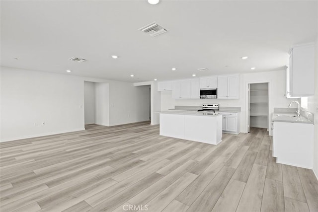 kitchen featuring a kitchen island, sink, white cabinets, light hardwood / wood-style floors, and electric stove