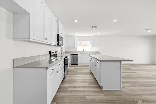 kitchen with sink, white cabinets, a center island, stainless steel appliances, and light hardwood / wood-style flooring