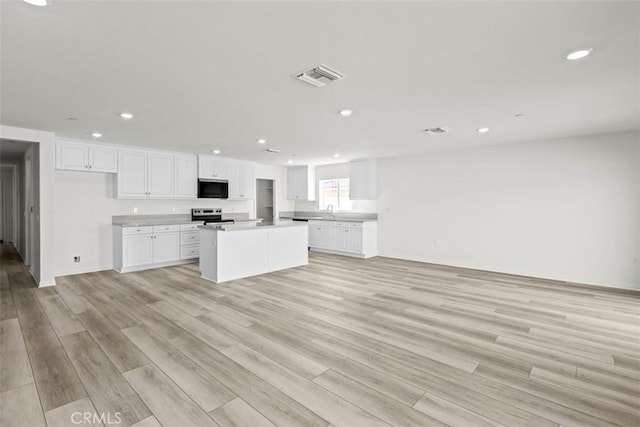 kitchen with a kitchen island, white cabinetry, sink, light hardwood / wood-style floors, and electric stove