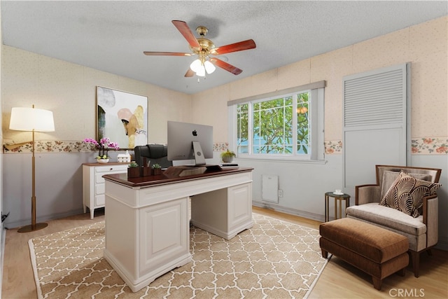 home office featuring light hardwood / wood-style floors, ceiling fan, and a textured ceiling