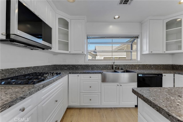 kitchen with dark stone counters, light wood-type flooring, sink, white cabinetry, and stainless steel appliances