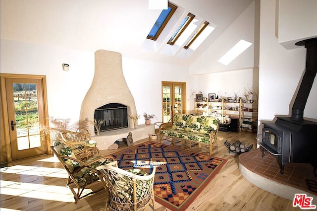 living room featuring hardwood / wood-style floors, a skylight, a wood stove, and high vaulted ceiling