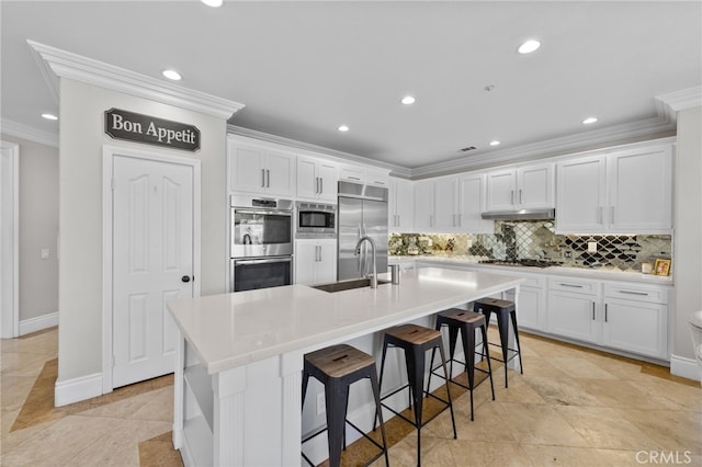 kitchen with white cabinetry, an island with sink, sink, and built in appliances