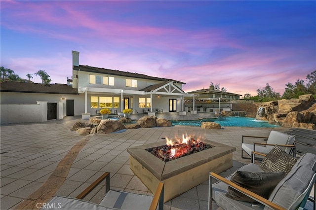 back house at dusk with pool water feature, a patio area, and an outdoor fire pit