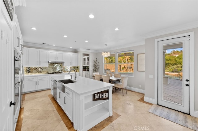 kitchen with pendant lighting, white cabinetry, an island with sink, sink, and decorative backsplash