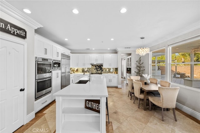 kitchen with built in appliances, hanging light fixtures, white cabinetry, and decorative backsplash