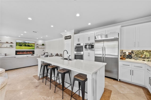 kitchen with sink, white cabinetry, a kitchen breakfast bar, built in appliances, and an island with sink