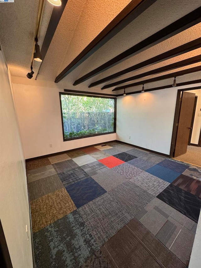 spare room featuring beam ceiling, dark colored carpet, and rail lighting