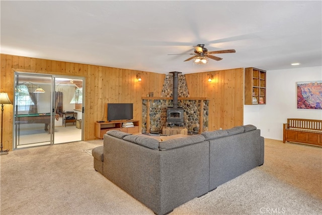 living room with carpet floors, wood walls, ceiling fan, and a wood stove