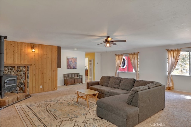 carpeted living room featuring wood walls, ceiling fan, and a wood stove