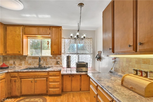 kitchen with light wood-type flooring, sink, an inviting chandelier, decorative backsplash, and decorative light fixtures