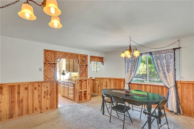 dining space featuring wooden walls, an inviting chandelier, and light colored carpet