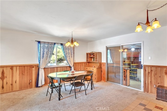 carpeted dining room featuring wooden walls and a notable chandelier