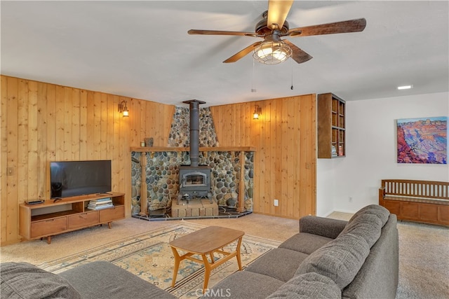 living room featuring light colored carpet, wood walls, ceiling fan, and a wood stove