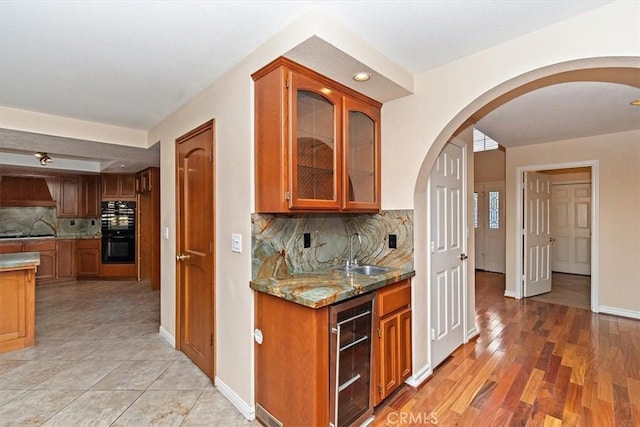 kitchen featuring decorative backsplash, light stone counters, sink, light hardwood / wood-style flooring, and wine cooler