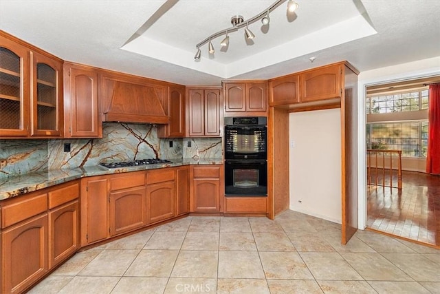 kitchen with light stone countertops, custom range hood, a tray ceiling, and stainless steel gas stovetop