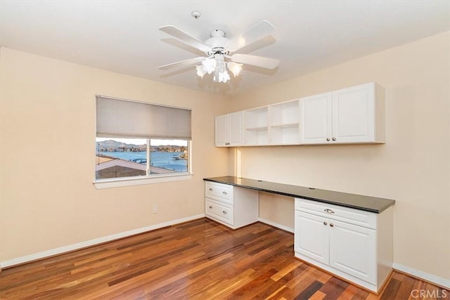 unfurnished office featuring built in desk, ceiling fan, and dark wood-type flooring