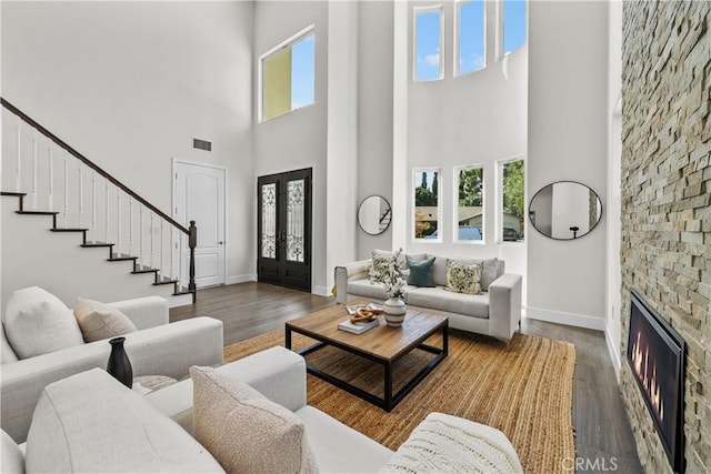 living room with a fireplace, dark hardwood / wood-style flooring, a towering ceiling, and french doors