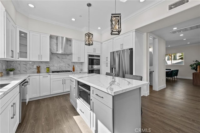 kitchen featuring white cabinetry, a kitchen island, wall chimney range hood, and appliances with stainless steel finishes