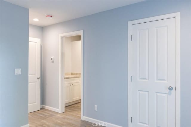 unfurnished bedroom with ensuite bathroom, light wood-style flooring, and baseboards