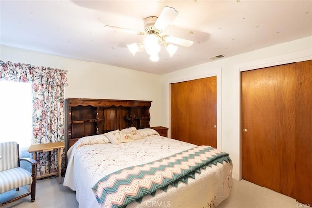 bedroom with a ceiling fan, light colored carpet, visible vents, and two closets