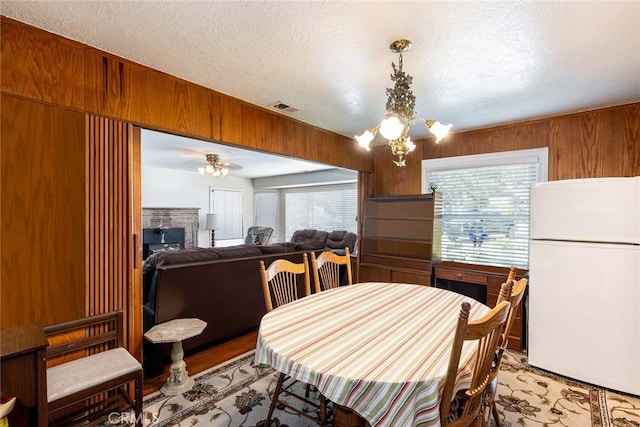 dining room featuring a notable chandelier, light wood finished floors, visible vents, wood walls, and a textured ceiling