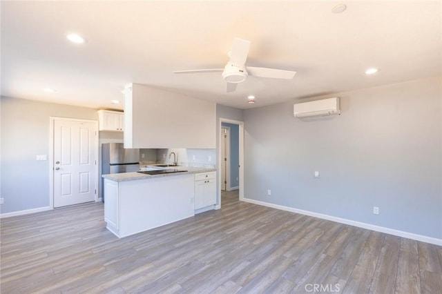 kitchen featuring freestanding refrigerator, an AC wall unit, white cabinets, and a sink