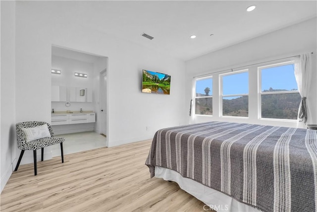 bedroom featuring connected bathroom and light hardwood / wood-style flooring